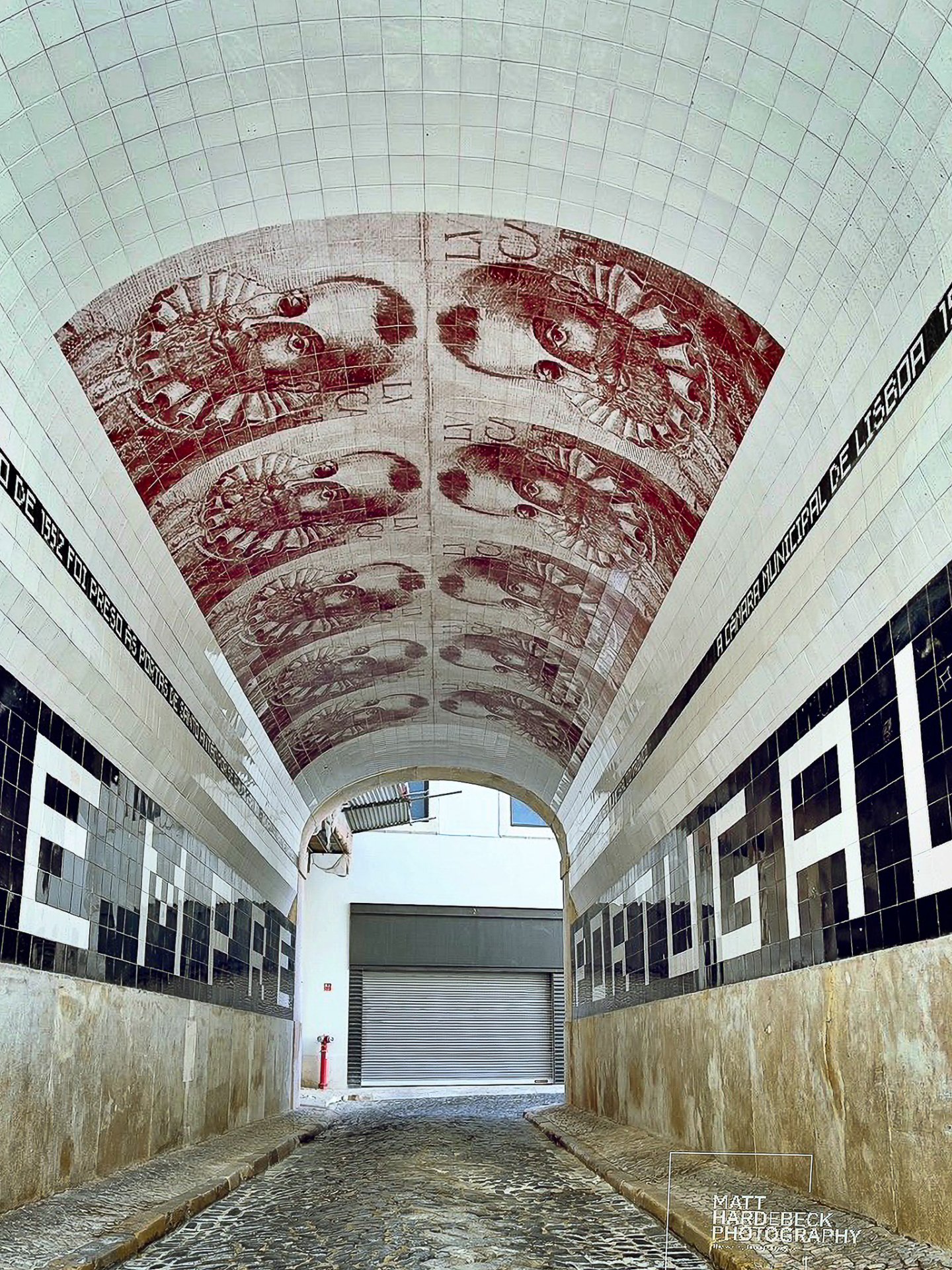 Arched passageway in Lisbon decorated with tiled portraits and the word “Portugal” in black and white tiles.