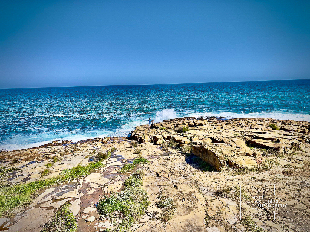 Rocky coastal cliffs at Luz with a lone figure standing near the crashing Atlantic waves.