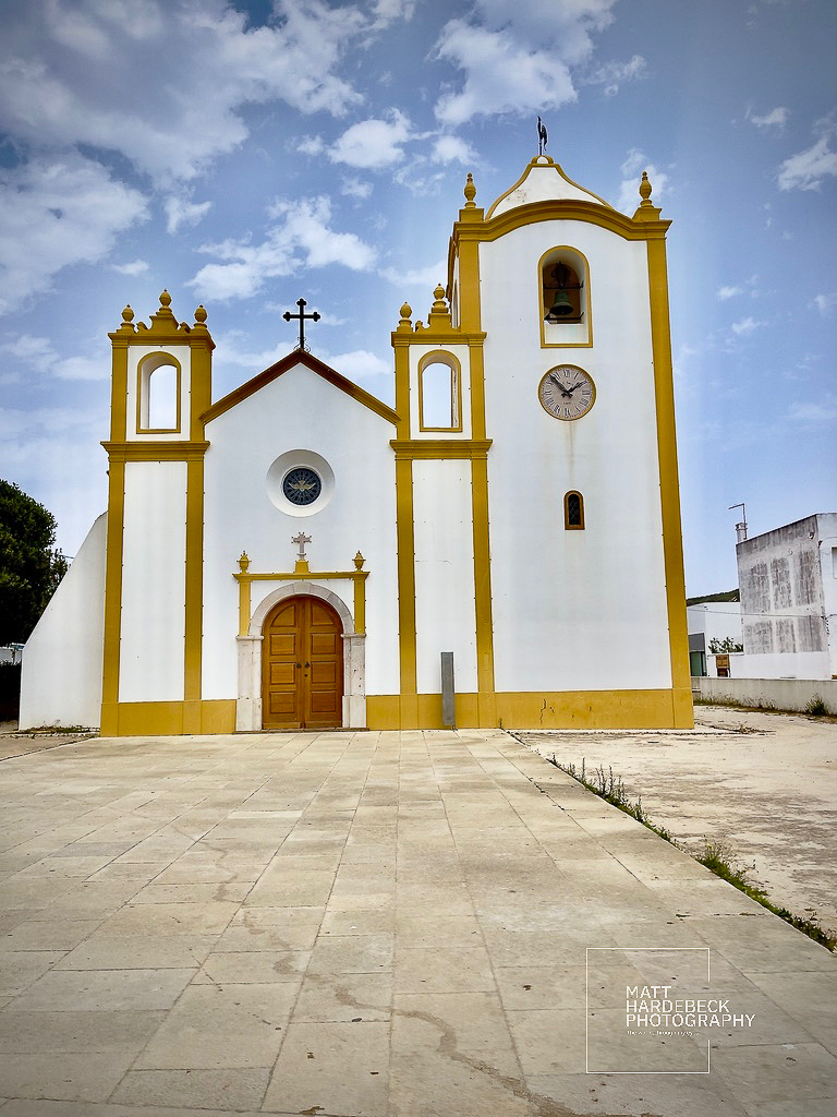 Whitewashed church with golden trim in Luz under a partly cloudy sky.
