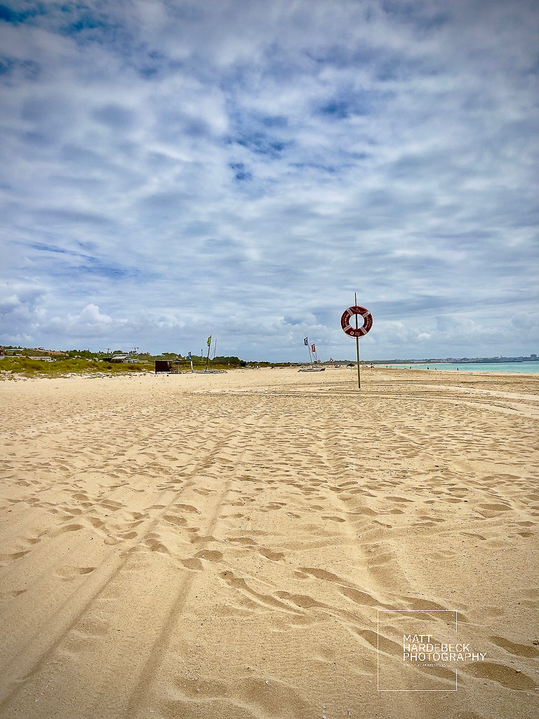 Wide expanse of Meia Praia beach with a lifebuoy station under a cloudy sky.