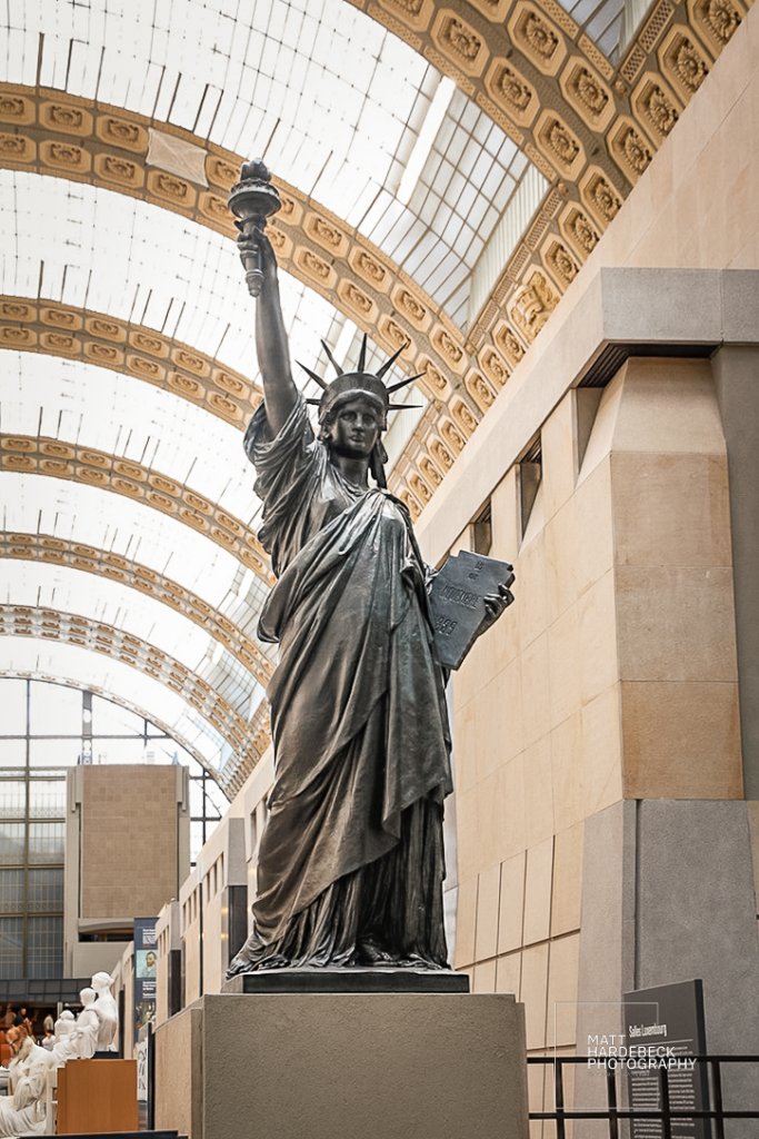 Bronze replica of the Statue of Liberty displayed inside the Musée d’Orsay, with the museum's arched glass roof in the background.