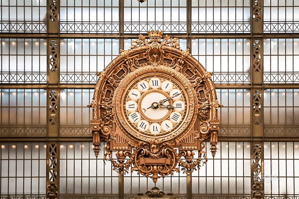 Ornate golden wall clock mounted above the entrance at the Musée d’Orsay, with Roman numerals and decorative flourishes.