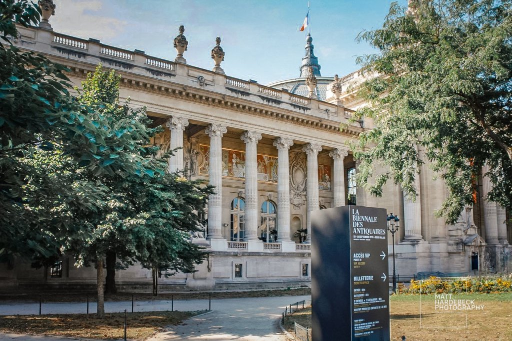 Neoclassical façade of the Grand Palais with columns and murals, seen from a garden path