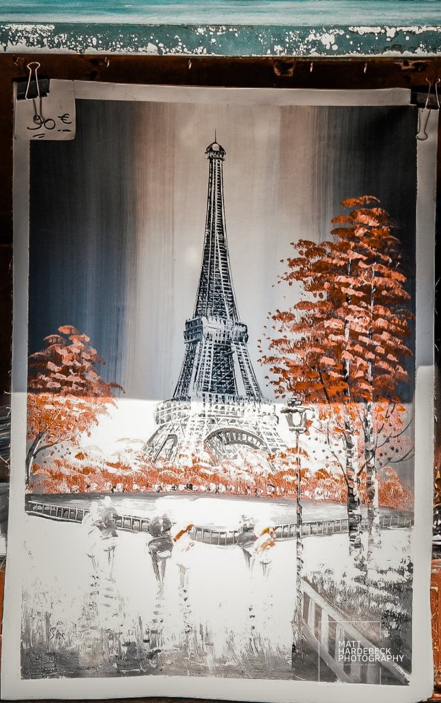 Painting of the Eiffel Tower with autumn trees and couples strolling by the Seine.
