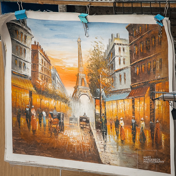 Vintage-style painting of the Eiffel Tower framed by Parisian streets and horse-drawn carriages.