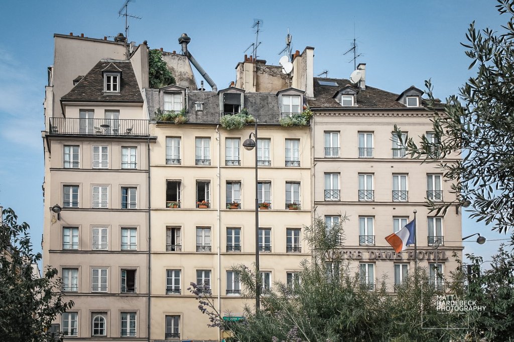 Historic buildings in Paris with window flower boxes and French flag on display.