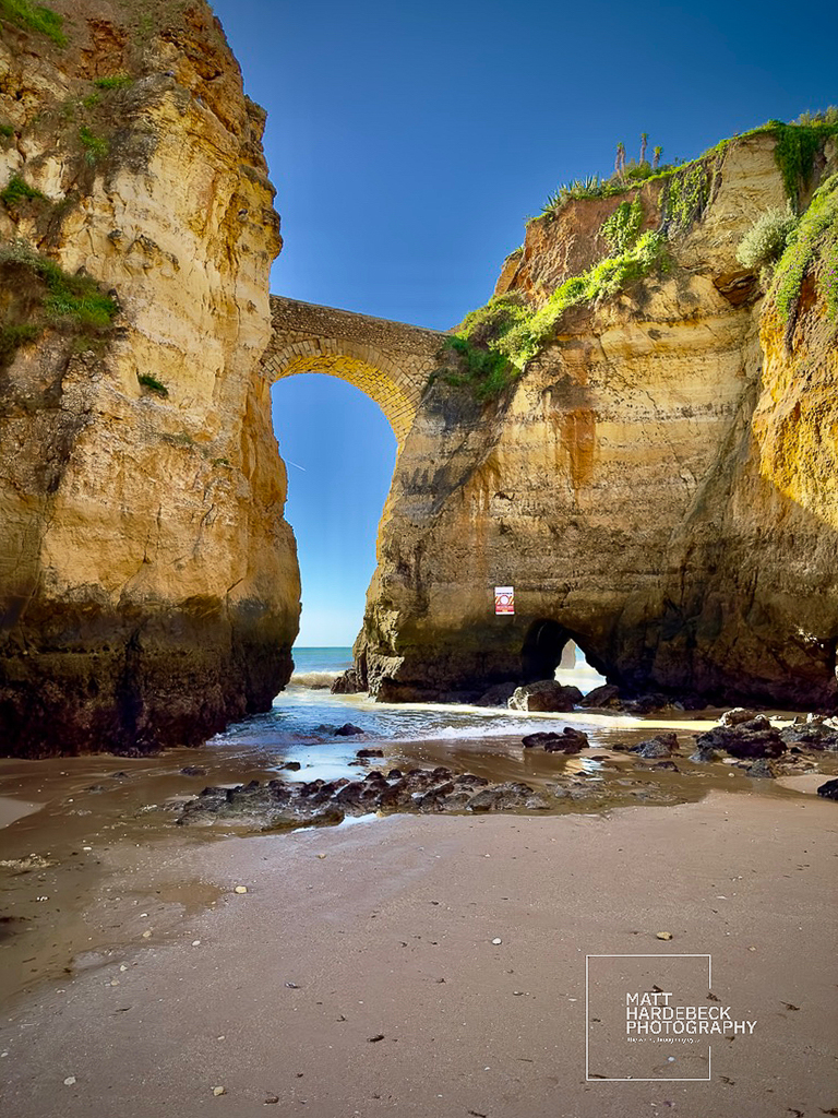 Stone arch bridge spanning two cliffs above a sandy cove in Lagos.