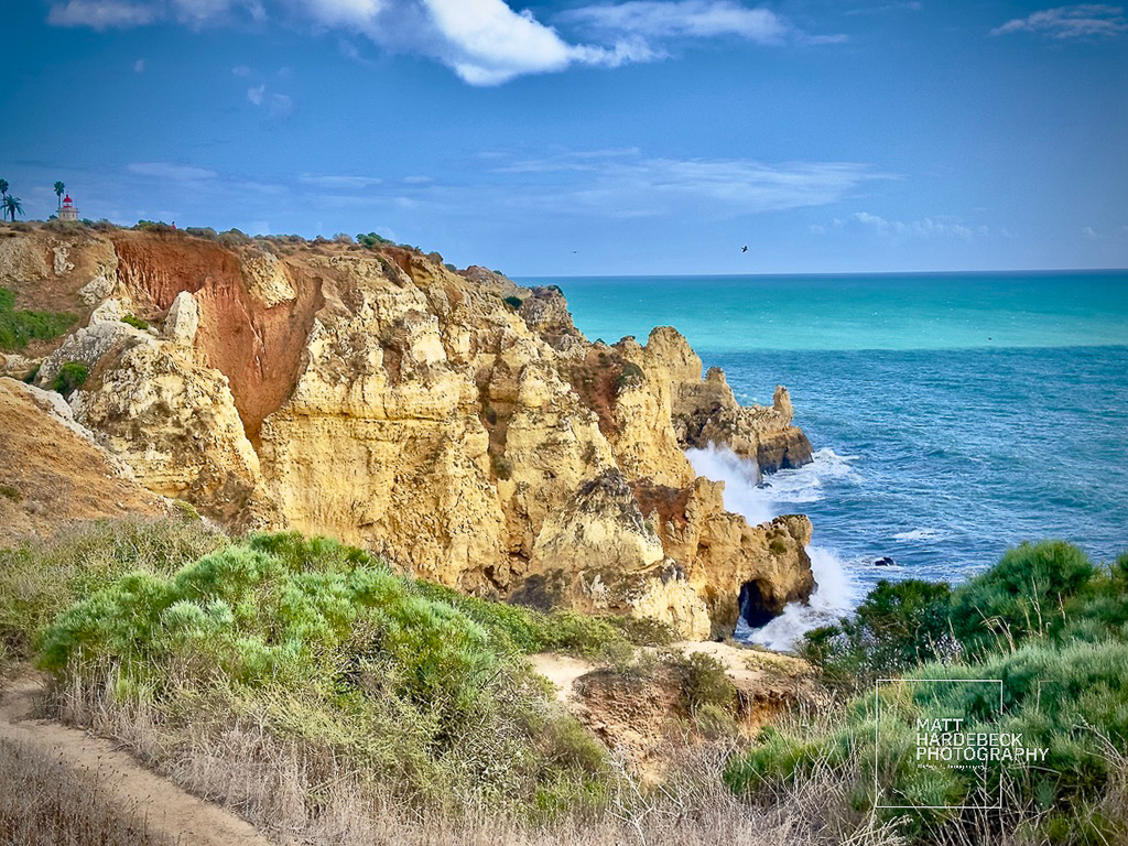 Waves crash against the base of the Ponta da Piedade cliffs with lighthouse in the distance.