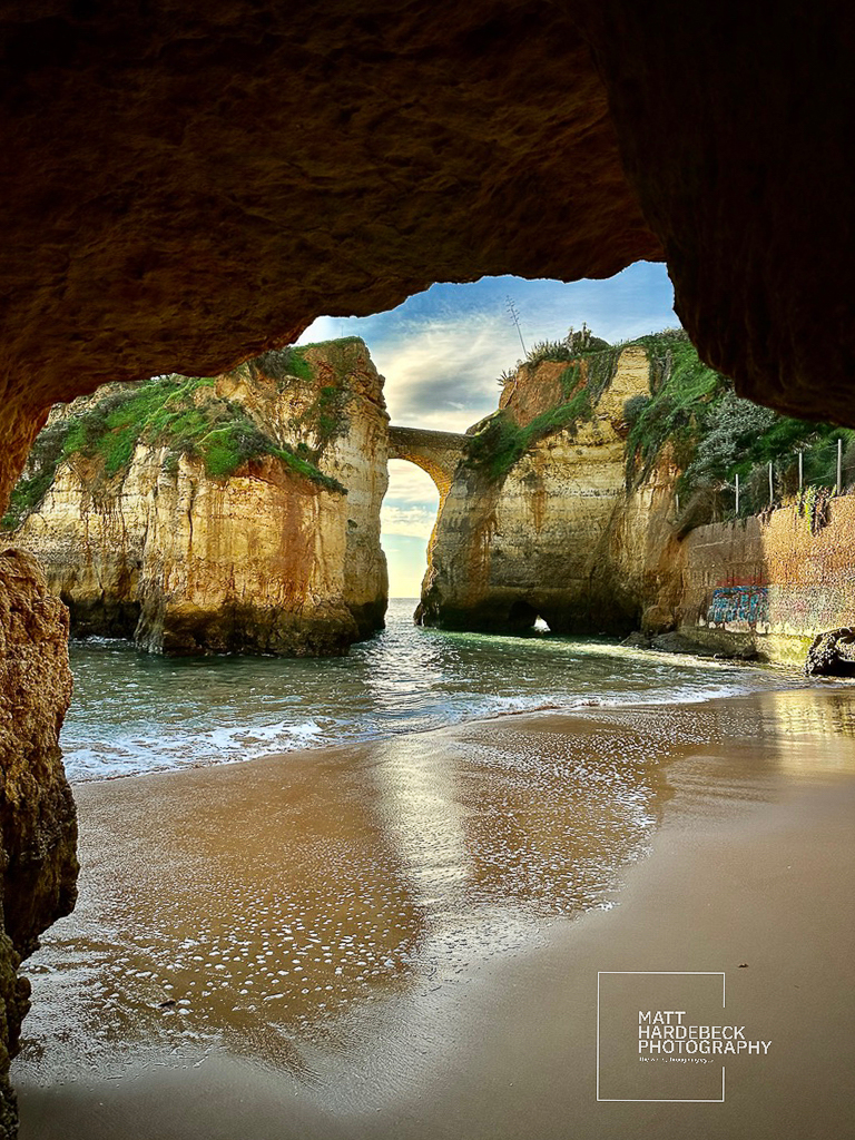 View from inside a coastal cave toward a stone arch and sandy beach in Lagos.