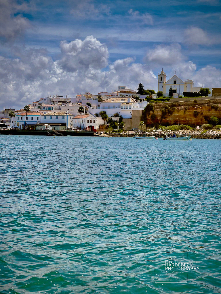 View of Ferragudo village and church from the water under a partly cloudy sky.