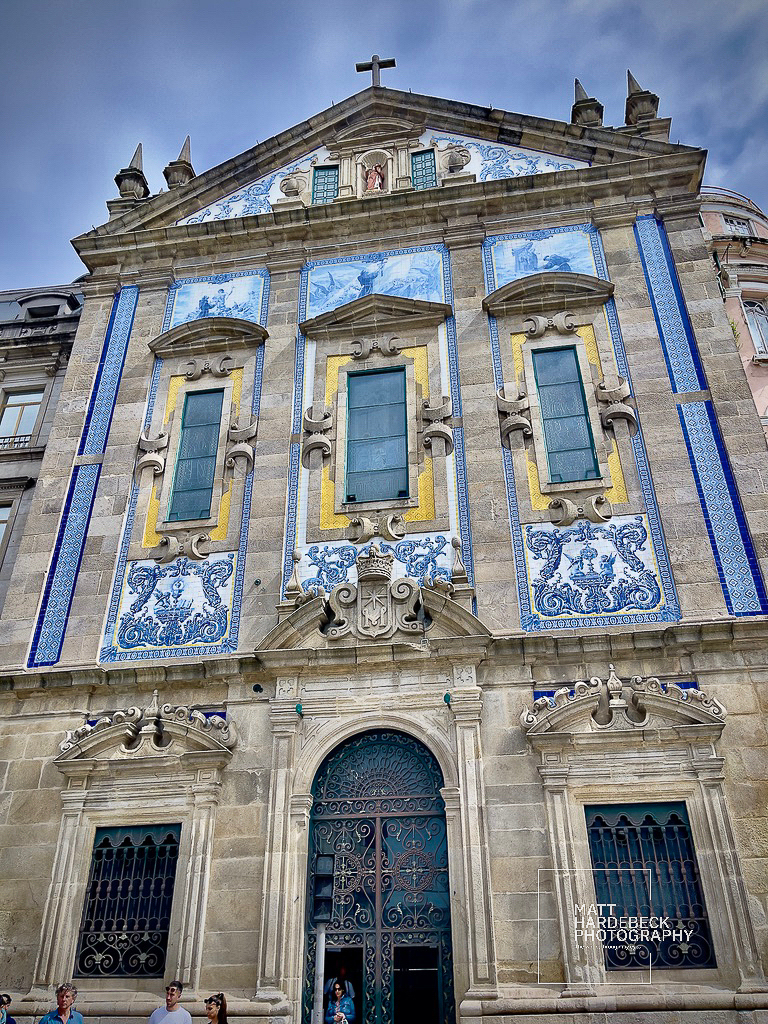 Facade of the Church of Saint Ildefonso in Porto, Portugal, adorned with blue-and-white azulejo tiles and Baroque architectural elements under a cloudy sky.