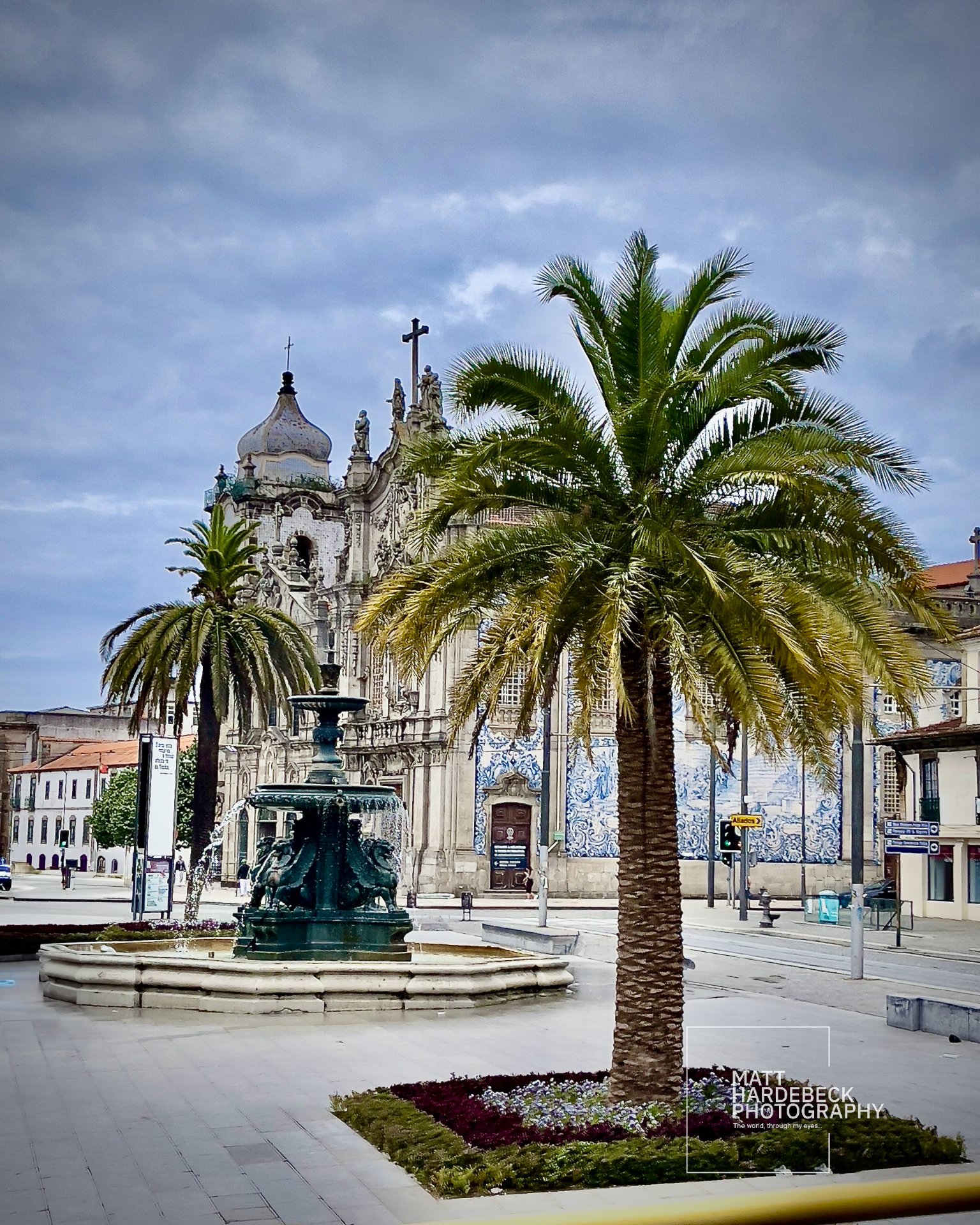 Fountain and palm trees in front of the Igreja do Carmo in Porto, Portugal, with its famous tiled facade visible in the background.