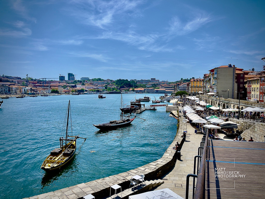 Boats docked along the Douro River waterfront in Porto, Portugal, with riverside cafes and colorful buildings lining the promenade.