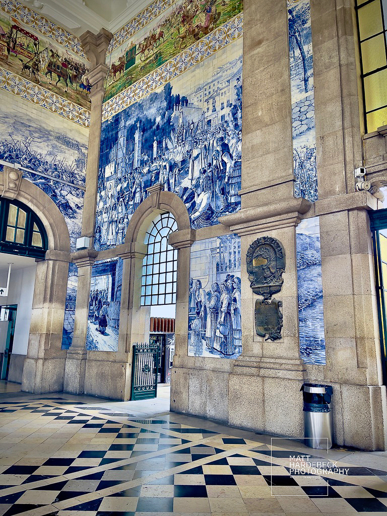 Interior of São Bento Railway Station in Porto, Portugal, with large blue-and-white azulejo murals depicting historical scenes.
