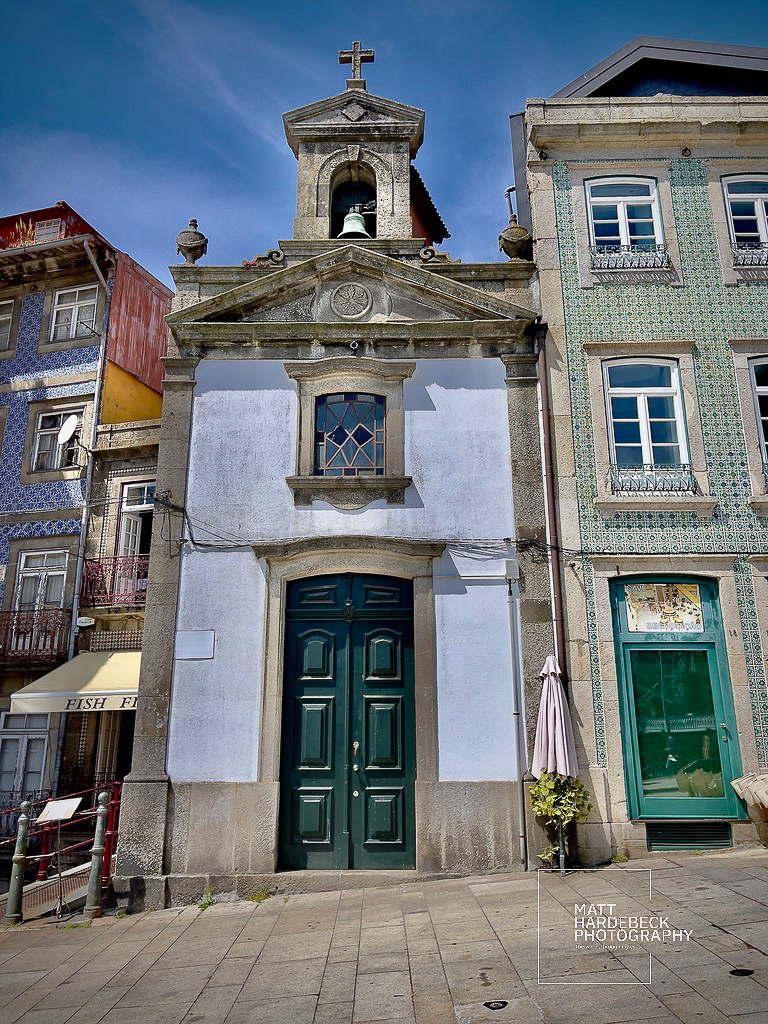 Small historic chapel with a bell tower in Porto, flanked by tiled buildings.
