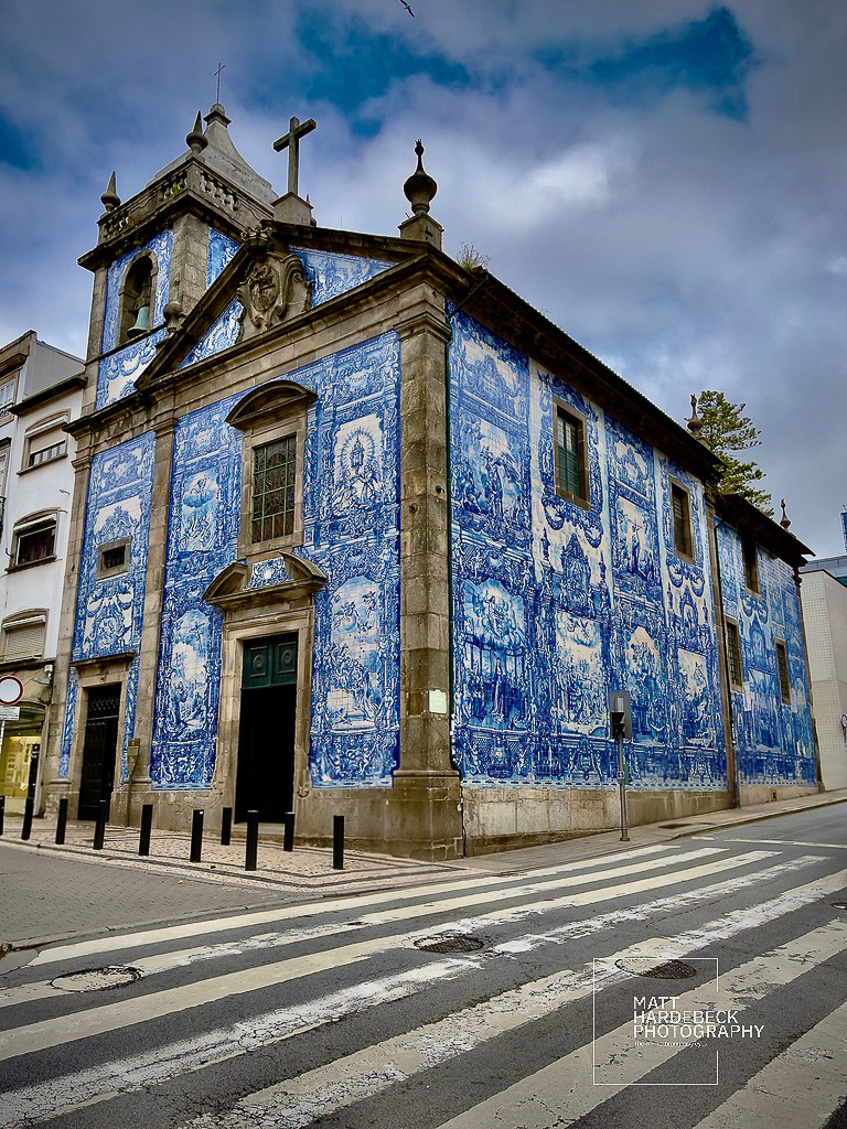 Exterior of Capela das Almas in Porto, Portugal, adorned with intricate blue-and-white azulejo tilework under a cloudy sky.