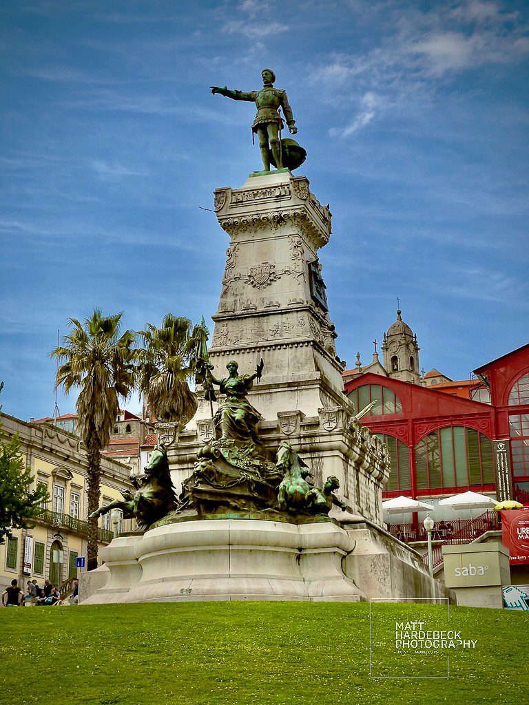 Monument to Prince Henry the Navigator in Porto, Portugal, with detailed bronze sculptures and palm trees in the background.