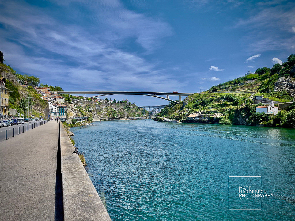 Riverside view in Porto, Portugal, with the Arrábida Bridge in the distance on a sunny day.