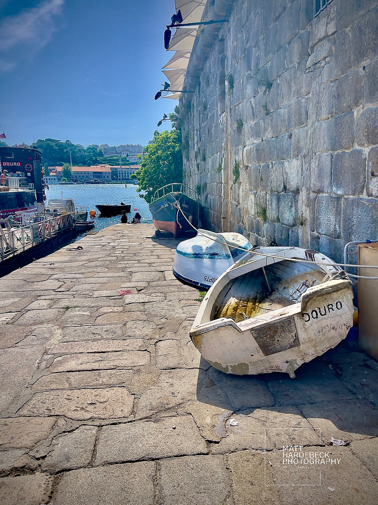 Weathered rowboats along the stone quay of Porto’s Ribeira district, with the Douro River in the background.