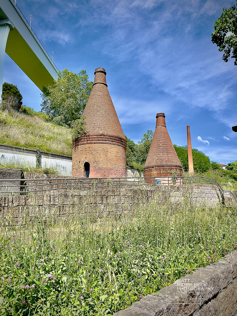 Historic brick kilns beneath a modern bridge in Porto, surrounded by greenery.