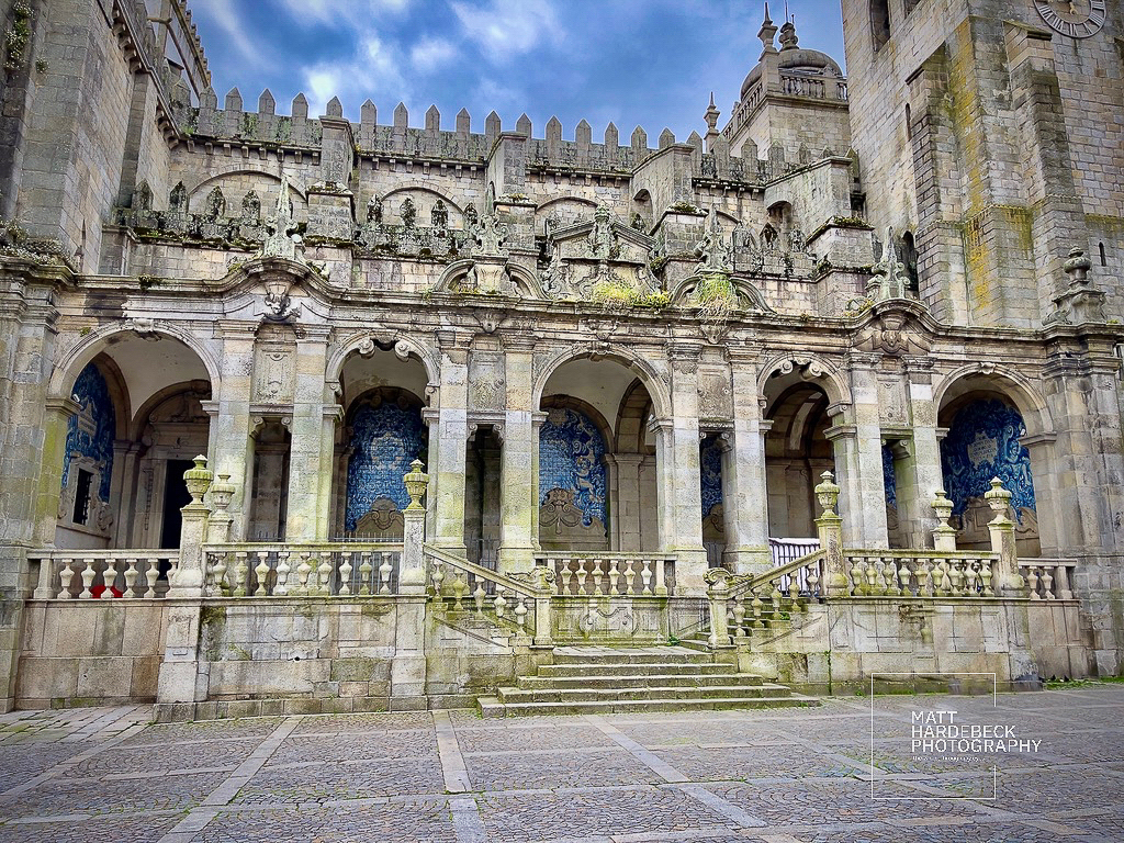 Stone cloister facade of Porto Cathedral with blue azulejo tilework visible through the arches.