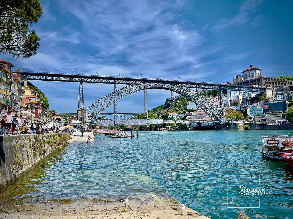 Dom Luís I Bridge spanning the Douro River, with colorful Ribeira buildings along the waterfront.