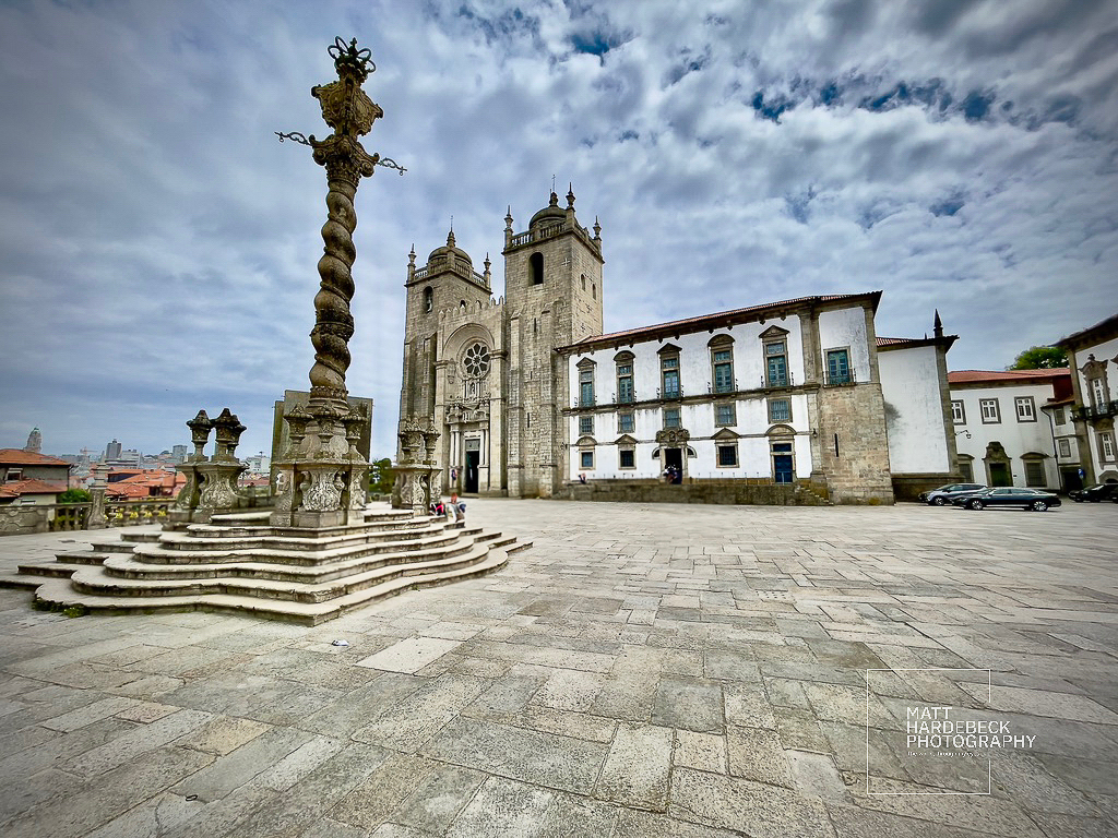 Exterior of Porto Cathedral and ornate pillory column under a partly cloudy sky.