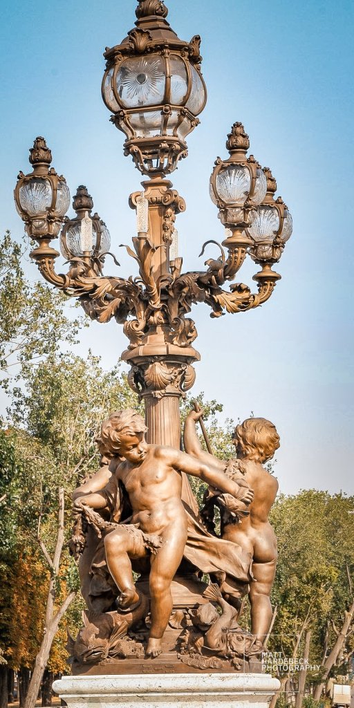 Ornate bronze street lamp with cherubic sculptures on the Pont Alexandre III in Paris.