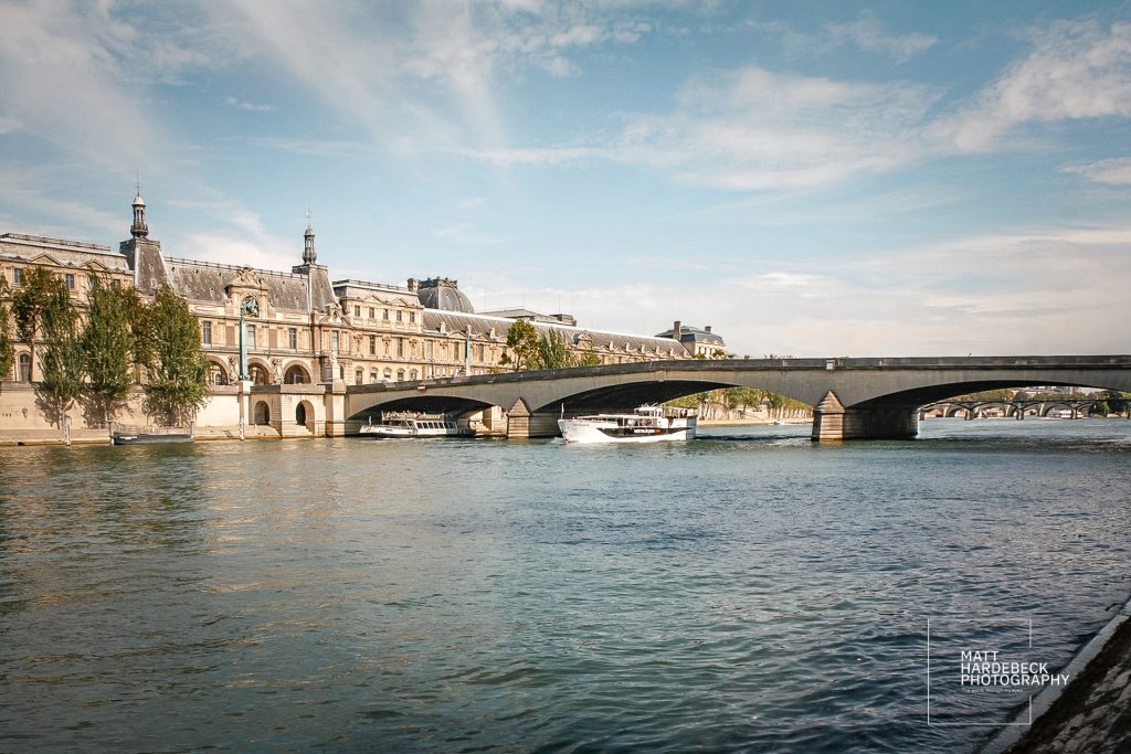 Wide view of the River Seine with a sightseeing boat and the Louvre building on the riverbank.
