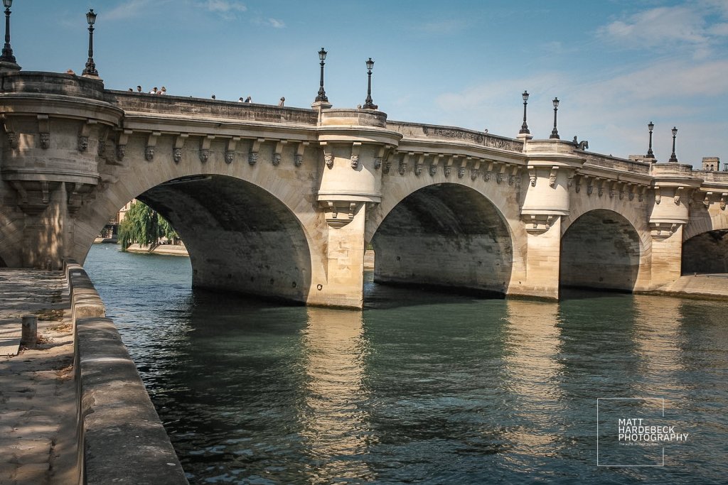 Pont Neuf bridge spanning the Seine, with visible arches and pedestrians on top.