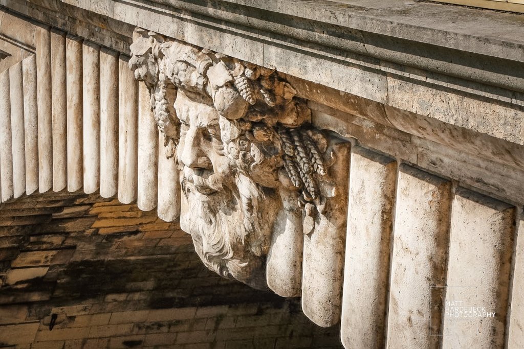 Sculpted stone head with grape leaves and a beard beneath a bridge on the Seine