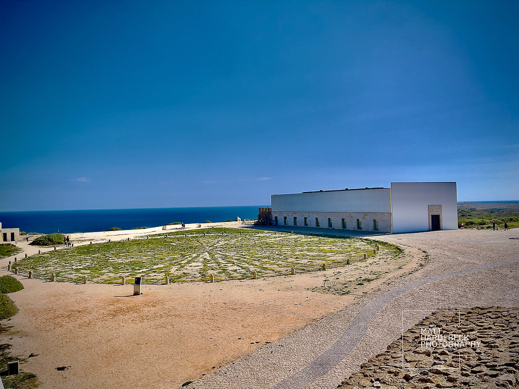 The 15th-century wind compass at Sagres Fortress, encircled by low stone markers under a vivid blue sky.