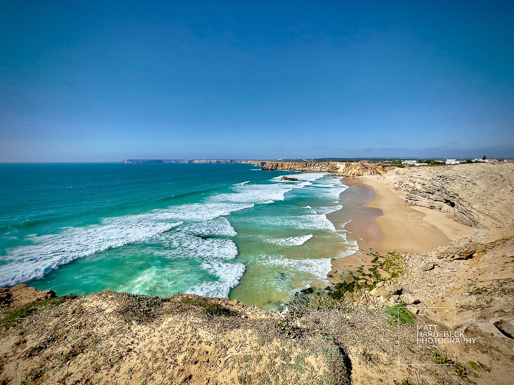 Panoramic view of sandy beach and turquoise waves beneath Sagres’ dramatic cliffs.