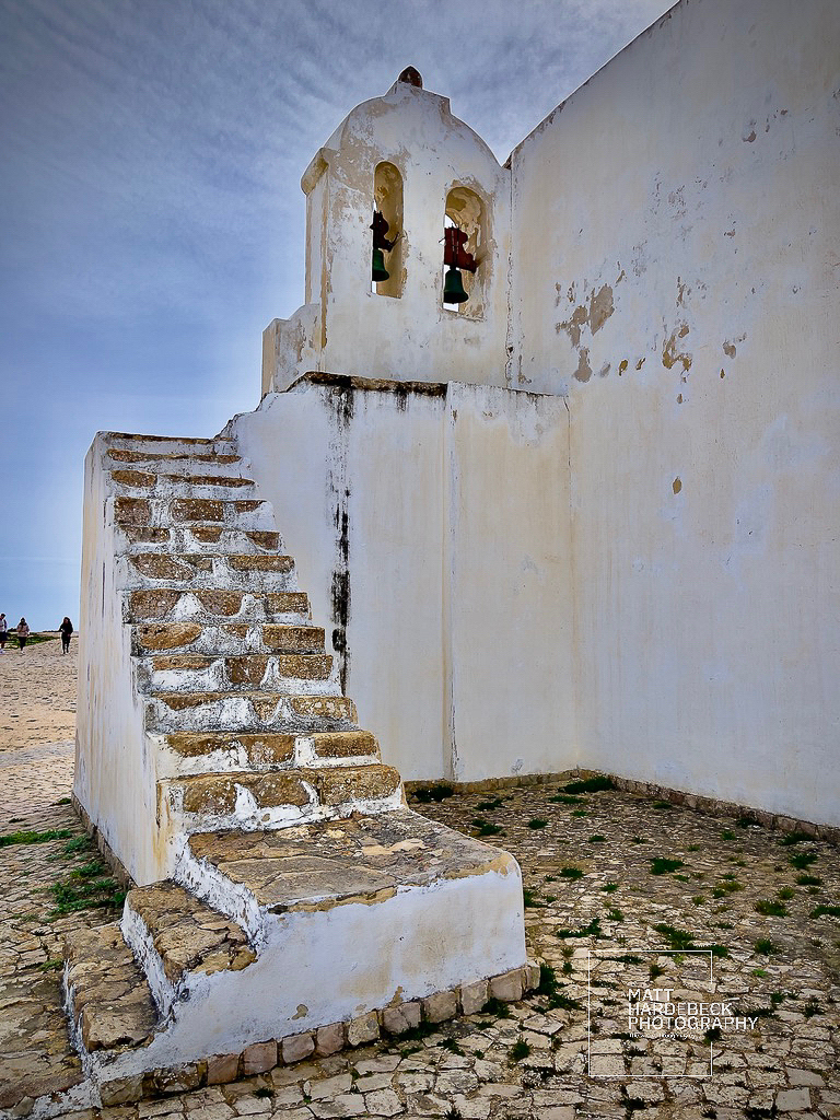 Weathered stone staircase leading to the bell tower of the whitewashed chapel at Fortaleza de Sagres, Portugal.