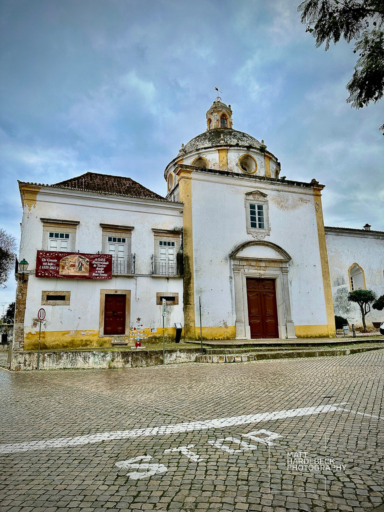 Whitewashed Baroque church with yellow trim and domed roof in Tavira’s historic center.