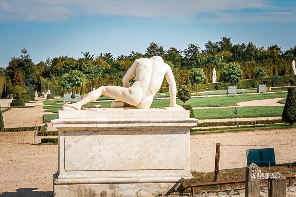 Classical nude male statue leaning forward on one arm in a manicured garden at Versailles.