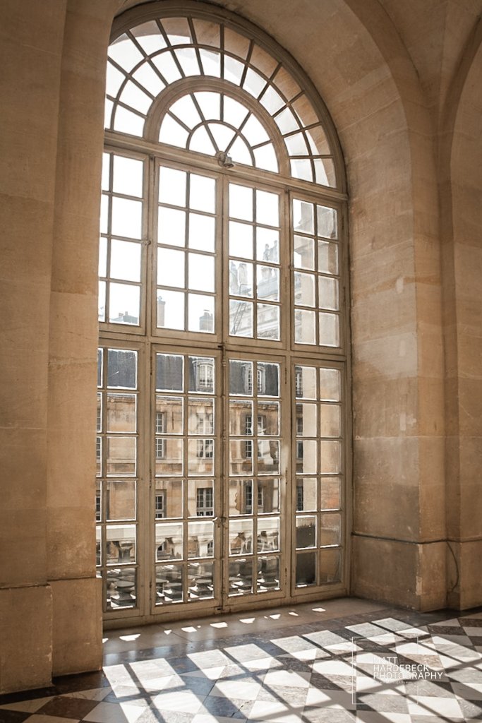 Large arched window with multiple panes, casting shadows onto a marble floor inside the palace.