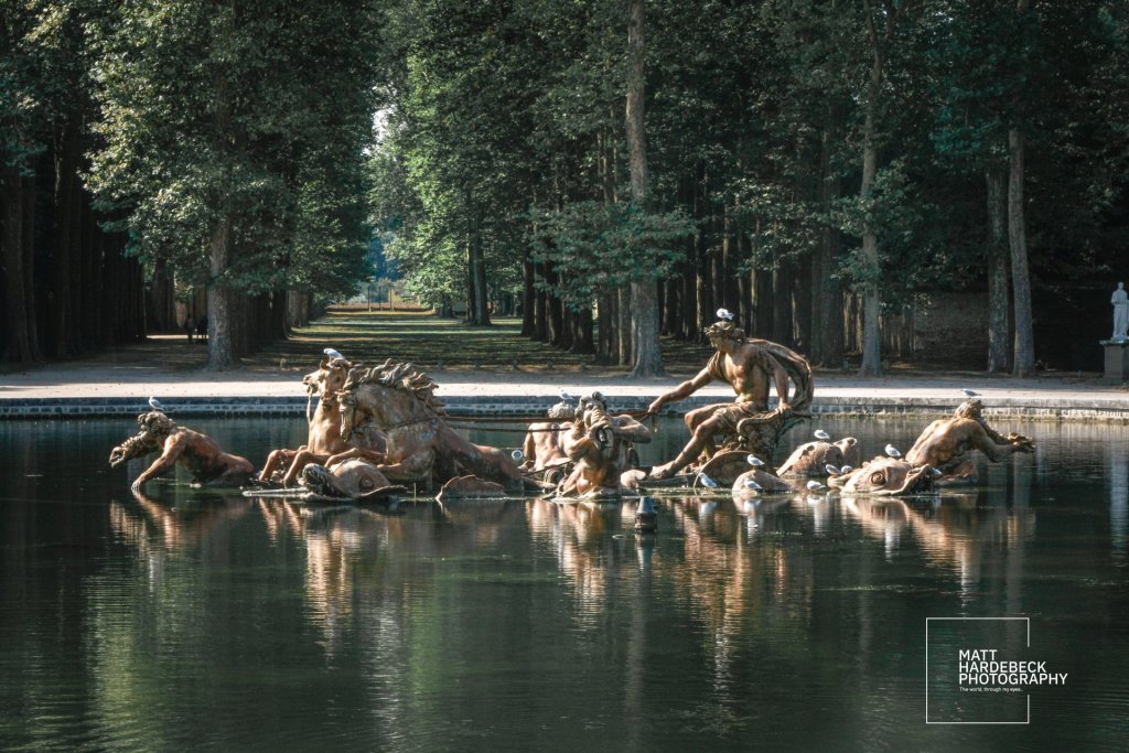 Detailed view of the bronze Apollo’s Chariot sculpture at Versailles, surrounded by trees and topped with perched seagulls.